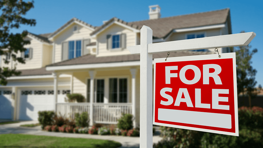 A For Sale sign hangs in front of a large two story home.