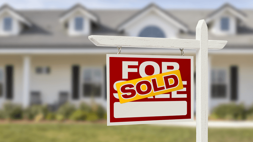 An image with a Sold sign in front of a ranch style home with four gables on the roof.